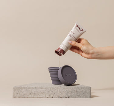 Hand pouring liquid from a DIVA bottle into a DIVA Shaker Cup on a beige background