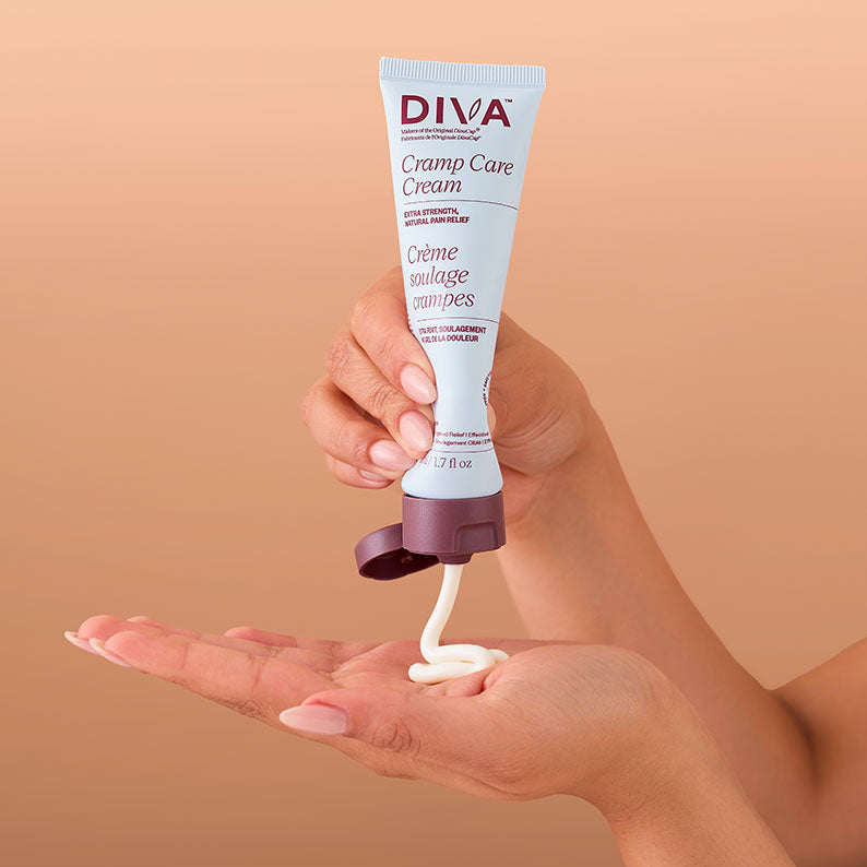 Hand holding a tube of Diva Cramp Care Cream against a beige background