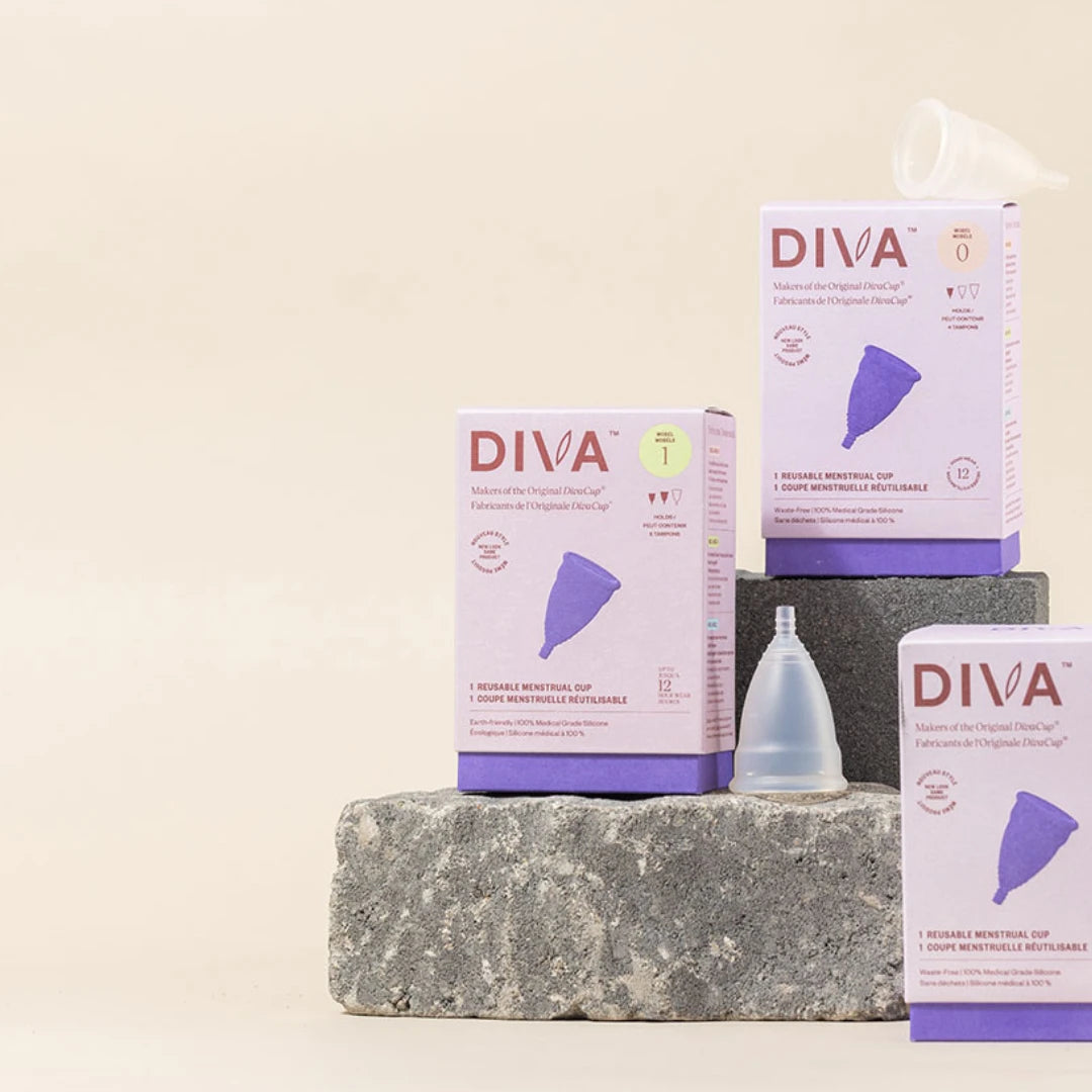 Three boxes of Diva menstrual cups and three clear menstrual cups are displayed on gray stone blocks against a beige background. 